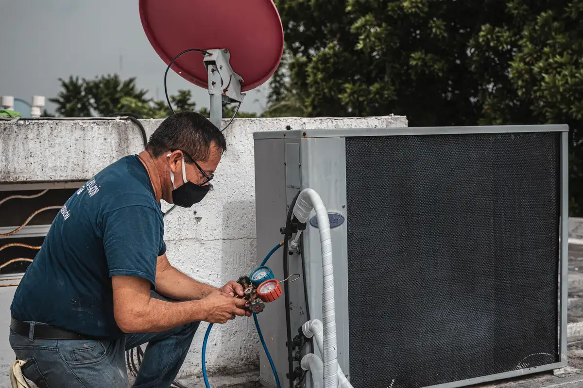 Technician in a face mask reading refrigerant gauges at a rooftop air conditioning unit