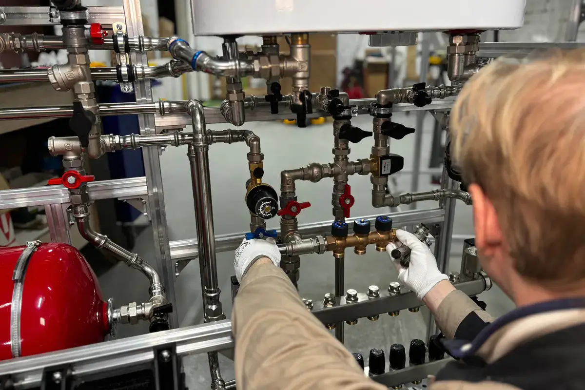 Gloved hands adjusting valves on a heating system's piping assembly