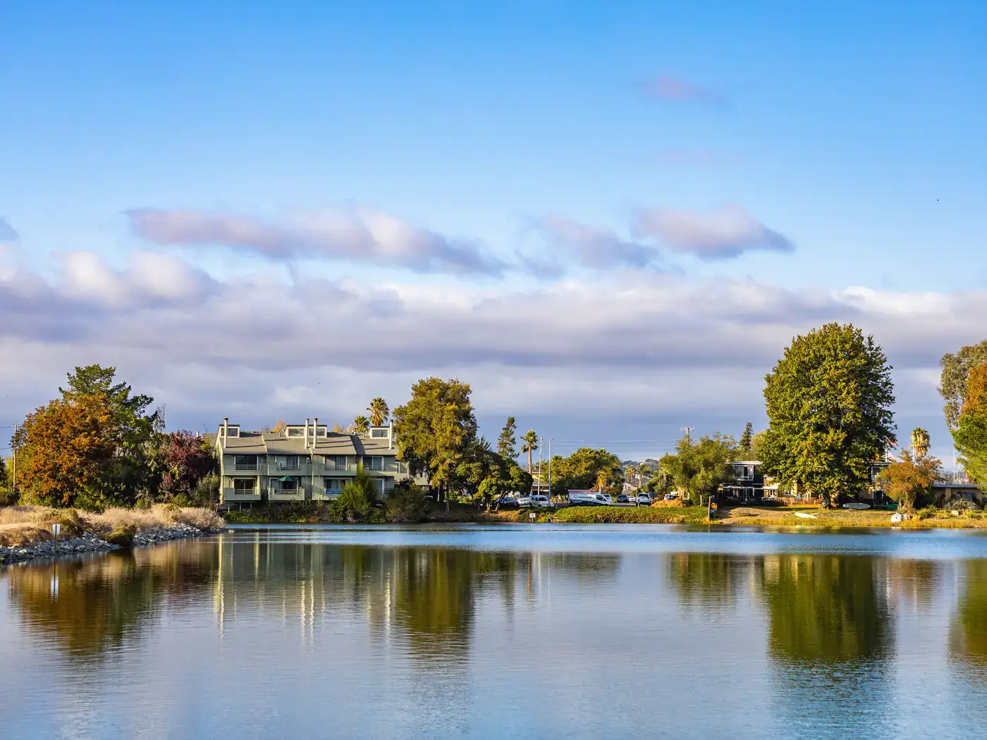 Homes among trees along the edge of a calm lake reflecting the sky