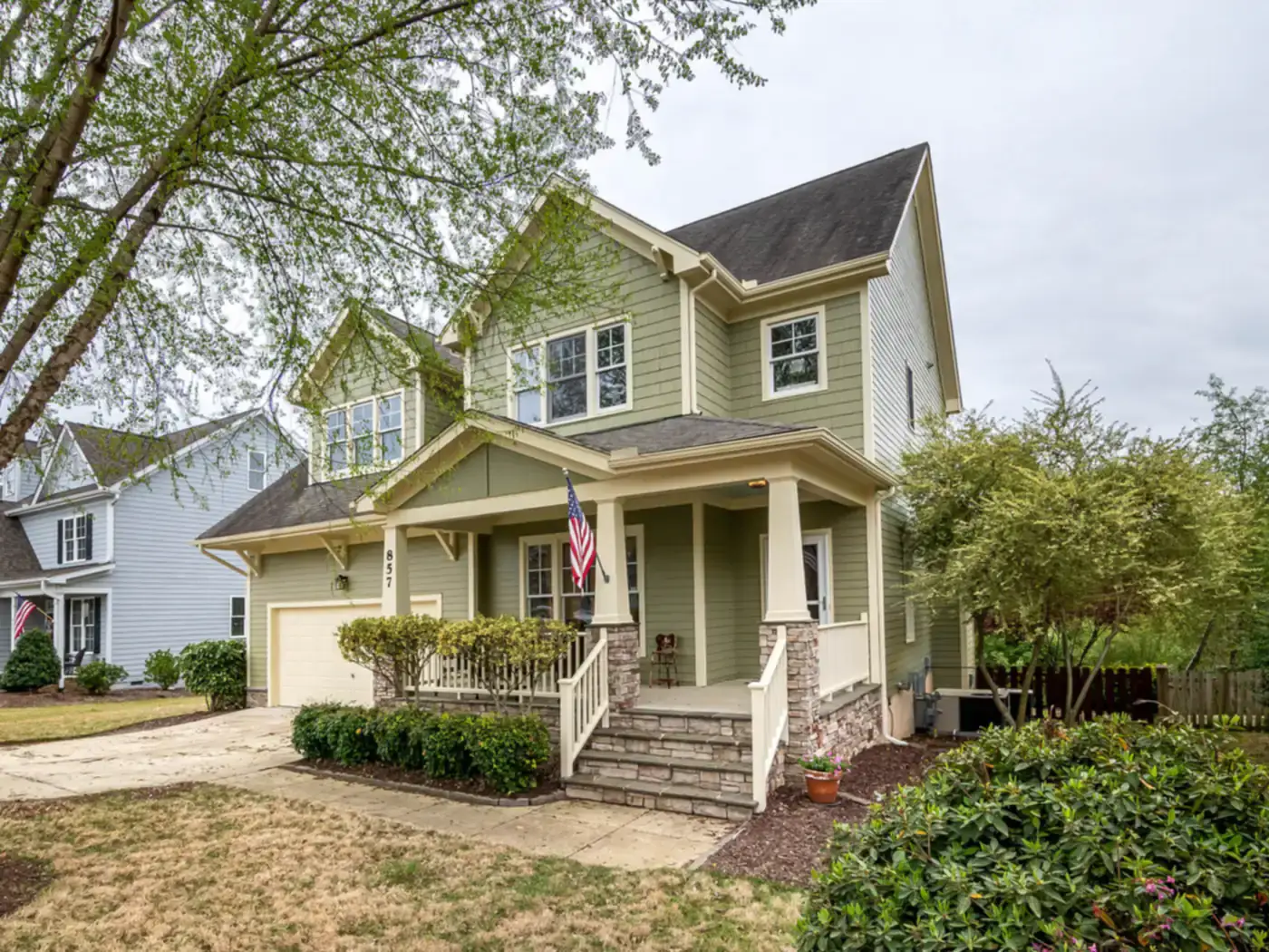 Two-story green house with a covered front porch and an outdoor air conditioning unit beside it