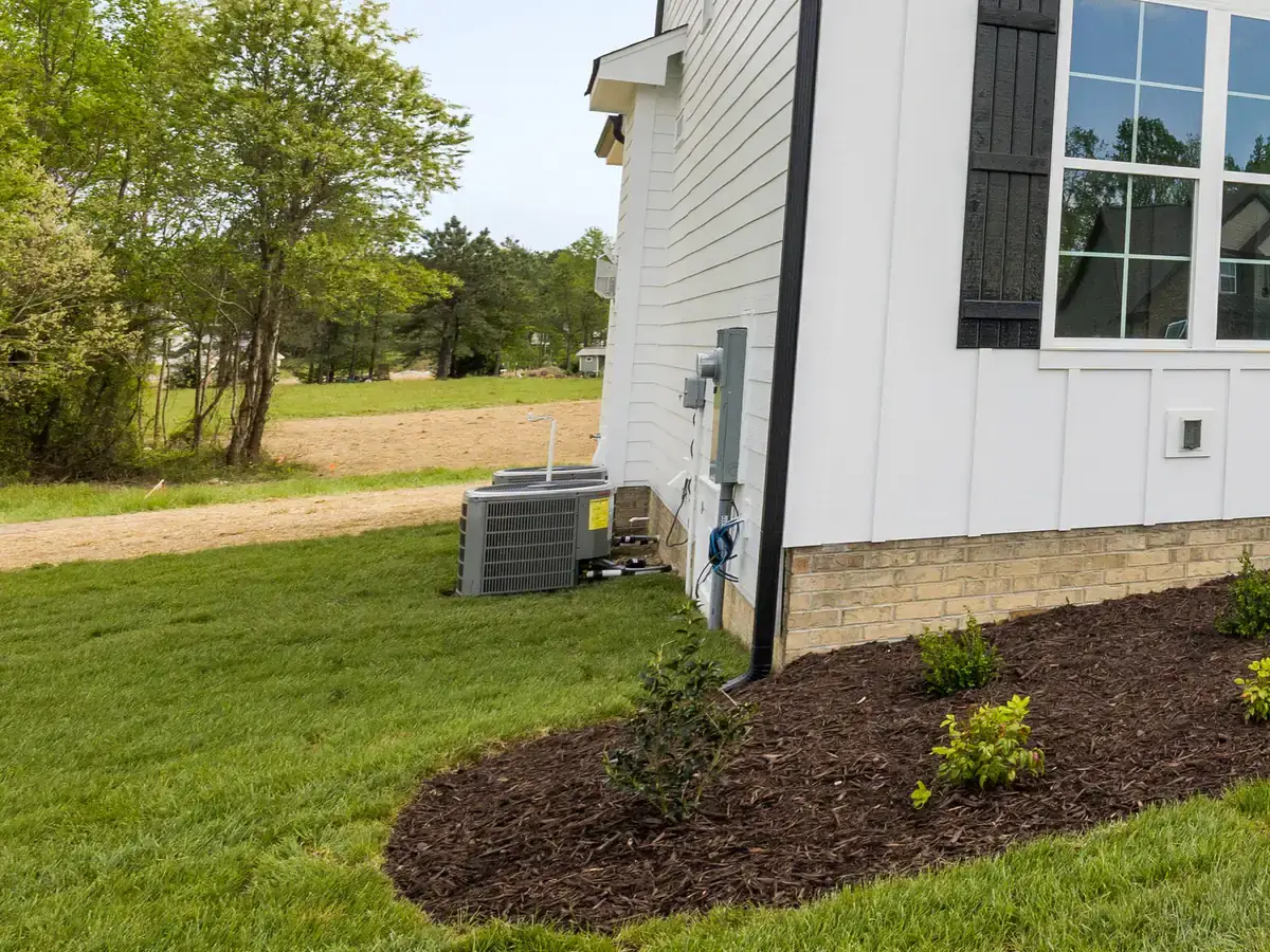Outdoor air conditioning units installed beside a new home with fresh mulch and lawn