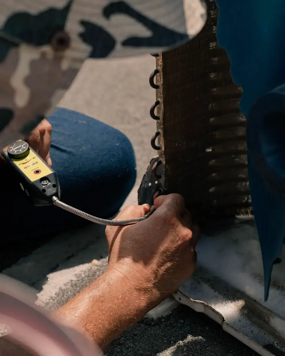 Close-up of a technician's hands testing an air conditioning coil with a meter probe