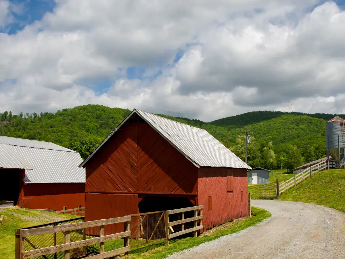Red barn beside a gravel road with green wooded hills behind