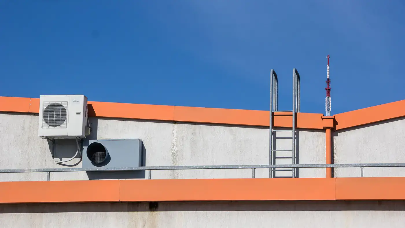 Outdoor air conditioning unit mounted on a rooftop wall under a clear blue sky