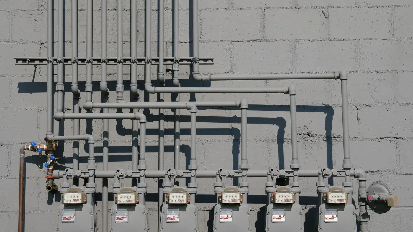 Row of gas meters with gray gas piping running up a block wall