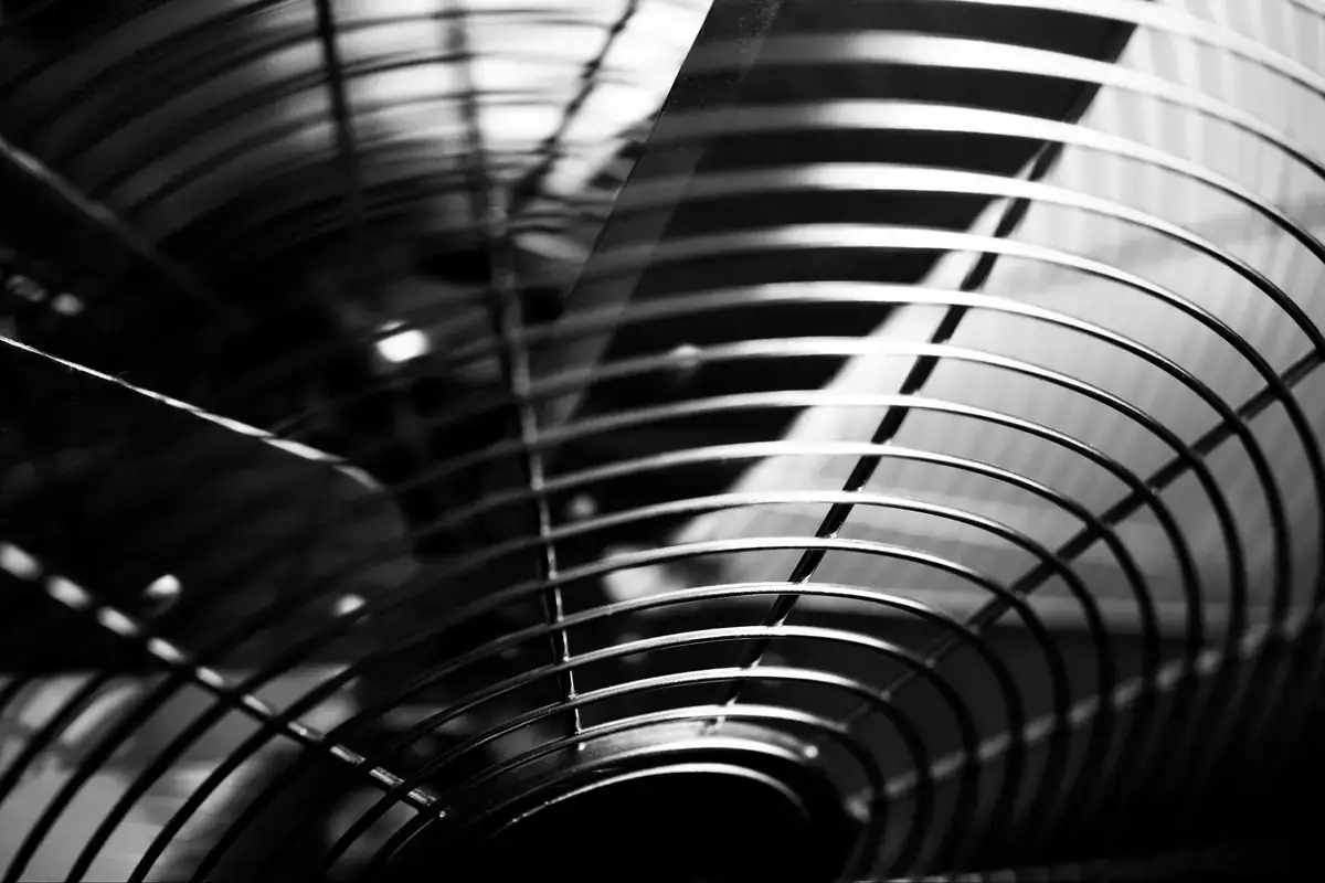 Black and white close-up of metal fan blades behind a round wire guard