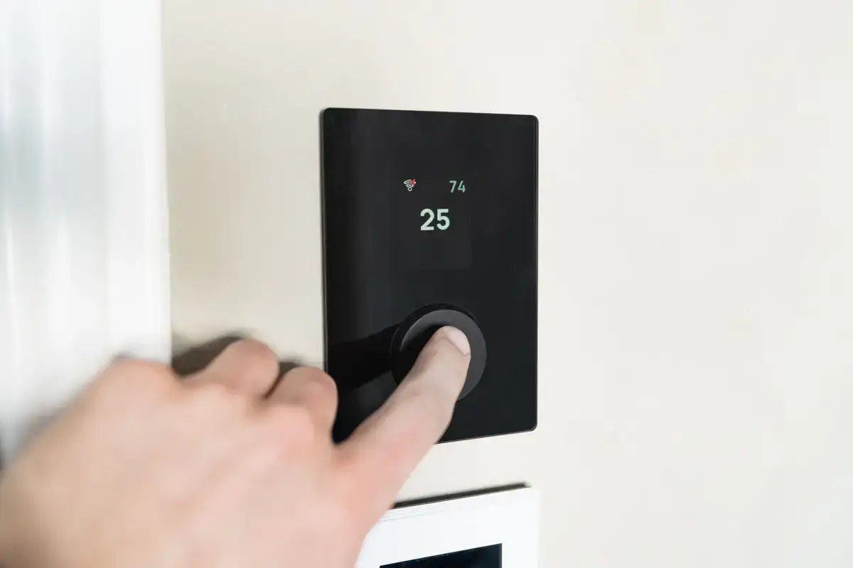 Hand pressing the dial on a black wall-mounted digital thermostat