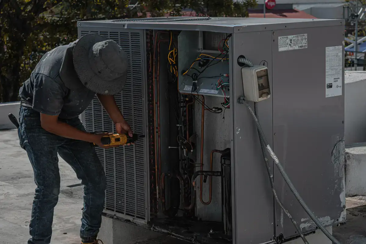 Technician using a meter on an open commercial air conditioning unit on a flat roof