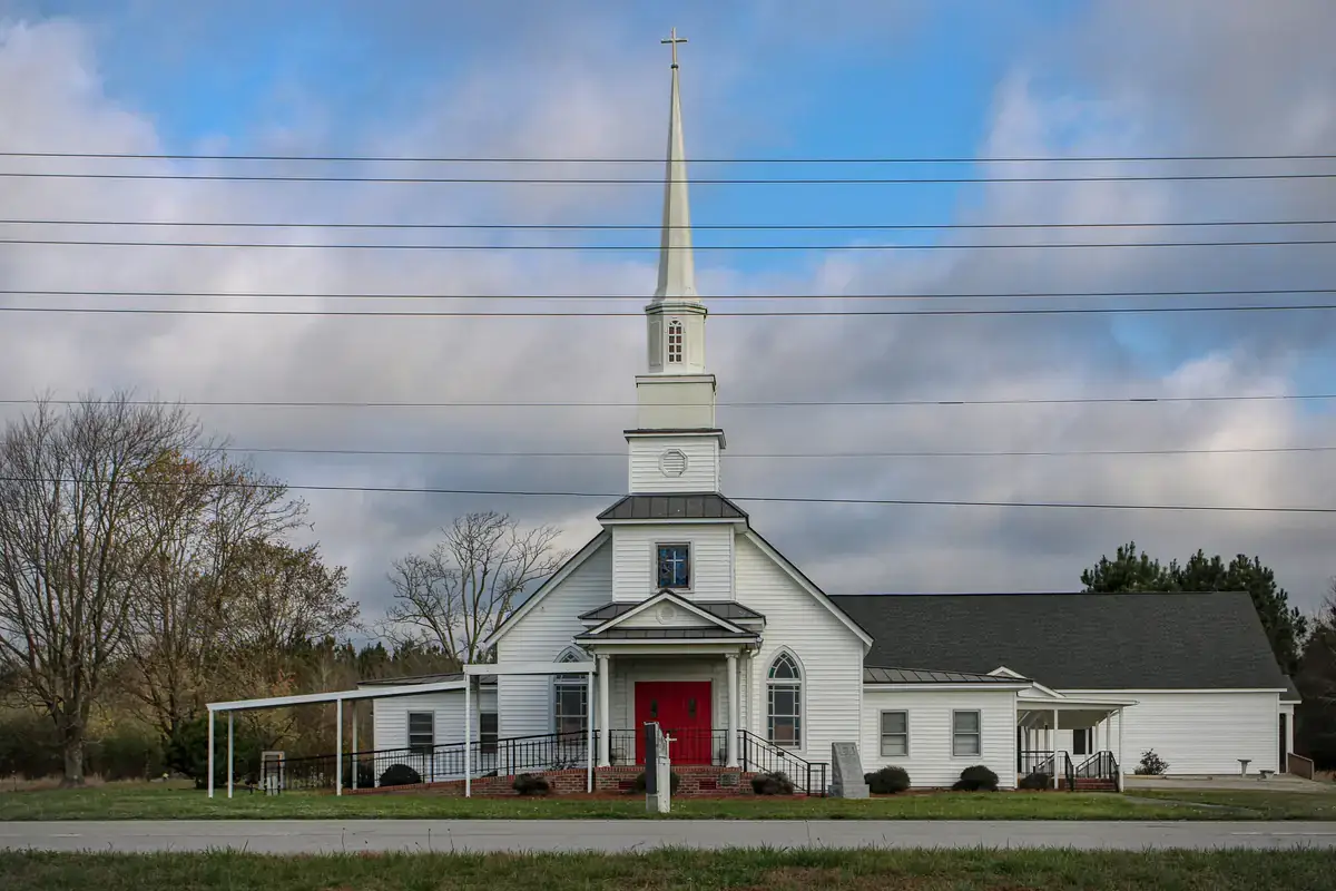 White church with a tall steeple and a red door beside a country road