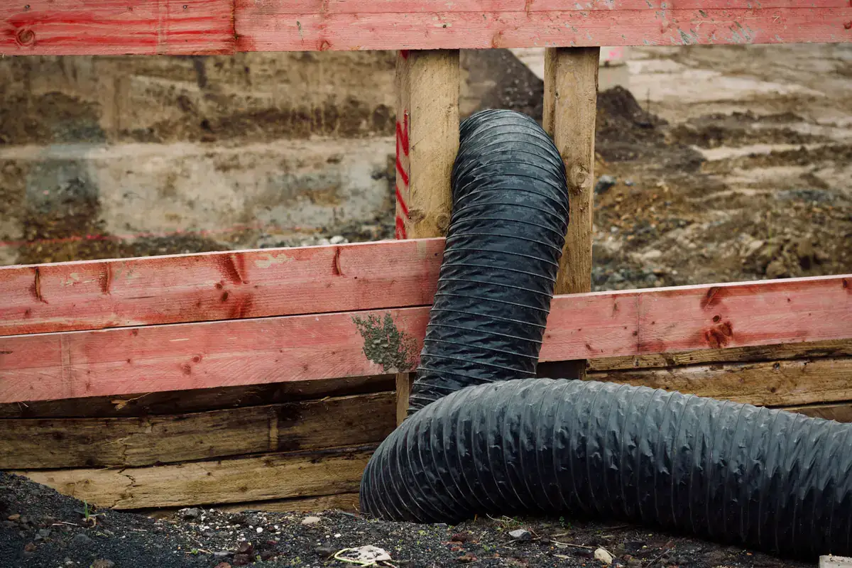 Black flexible duct hose running through a wood-framed opening at a construction site