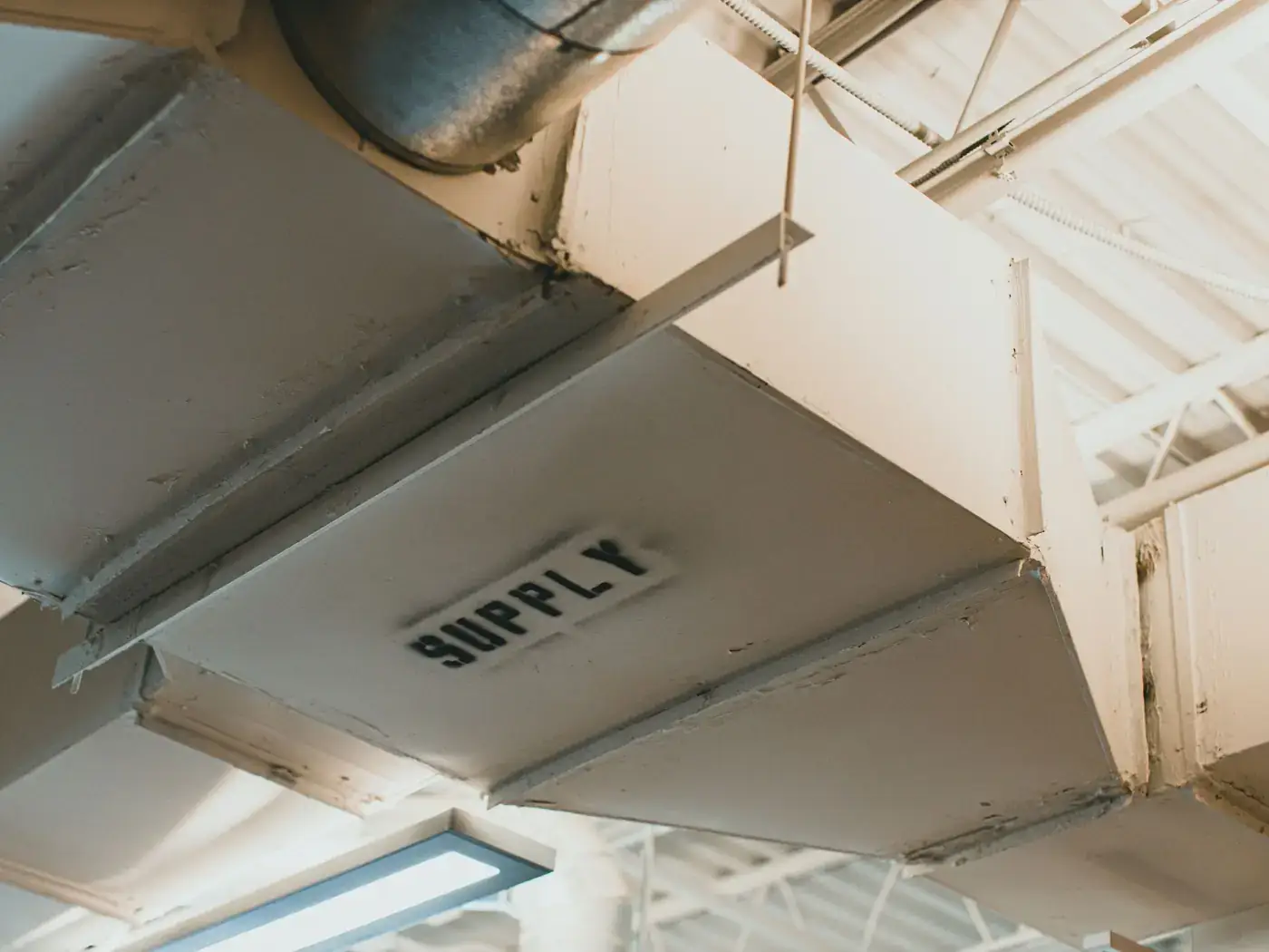 Sheet-metal supply ductwork running along a ceiling, stenciled with the word SUPPLY