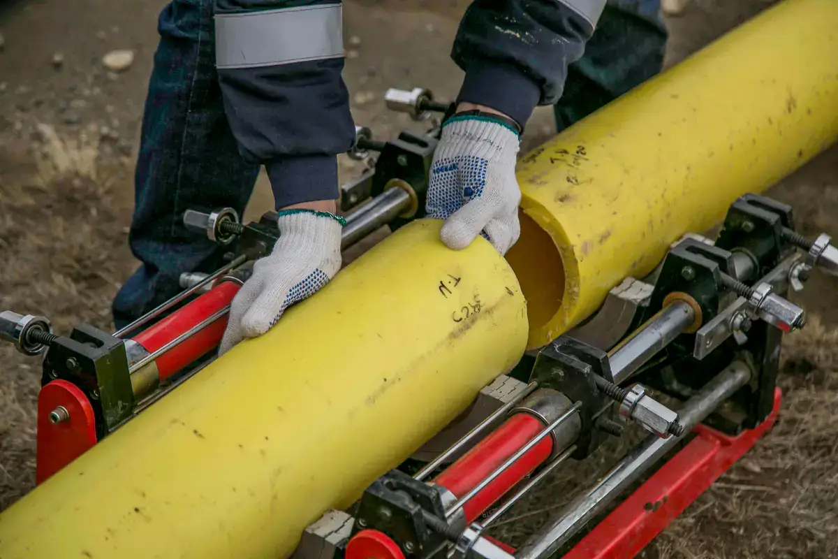 Gloved hands setting a length of yellow plastic gas pipe into a pipe clamping machine