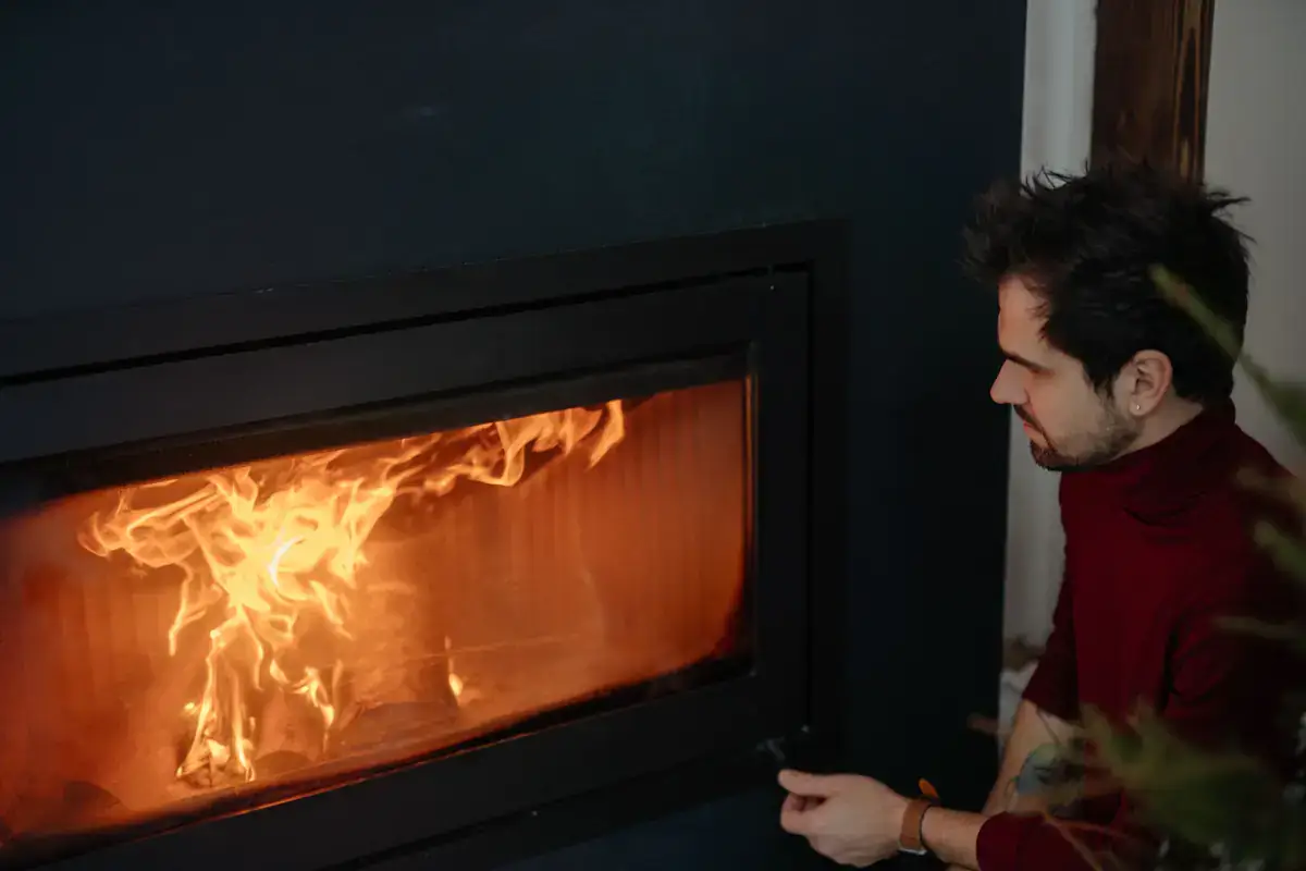 Man adjusting a modern fireplace insert with a wide glass front and flames