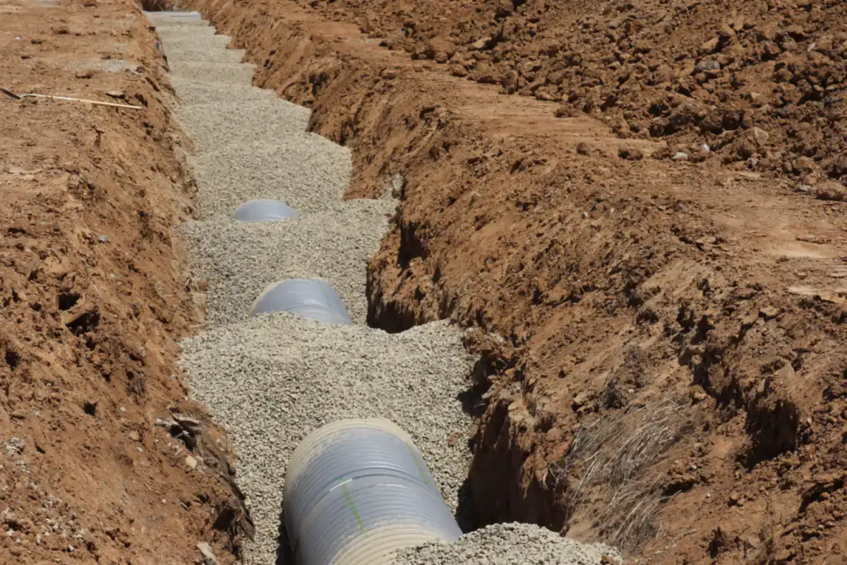 Large plastic pipe laid in a gravel-lined trench dug through red clay soil