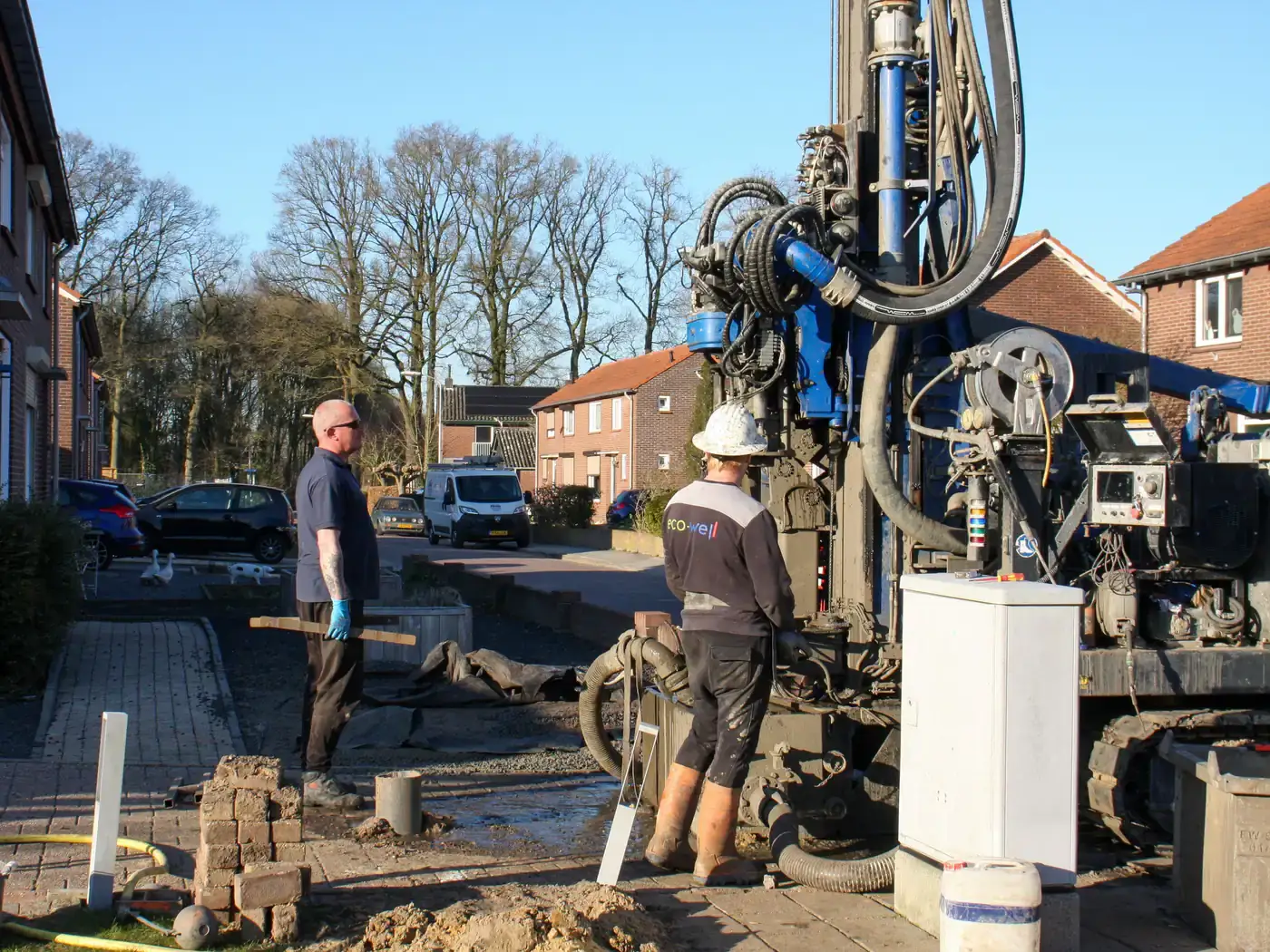 Crew operating a drilling rig to bore a well beside a brick home