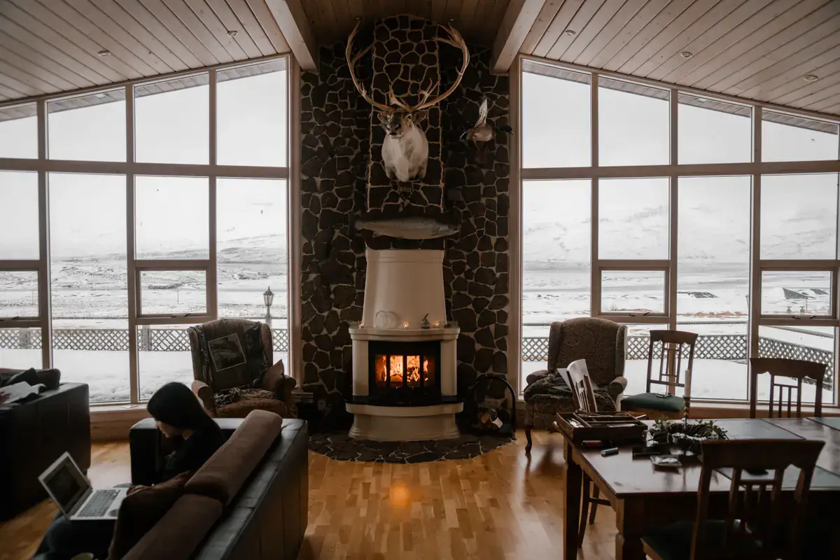 Warm living room with a lit fireplace and tall windows looking out on snow