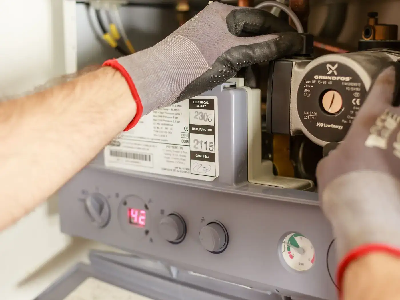 Gloved hands adjusting the circulator pump and controls inside an open heating unit
