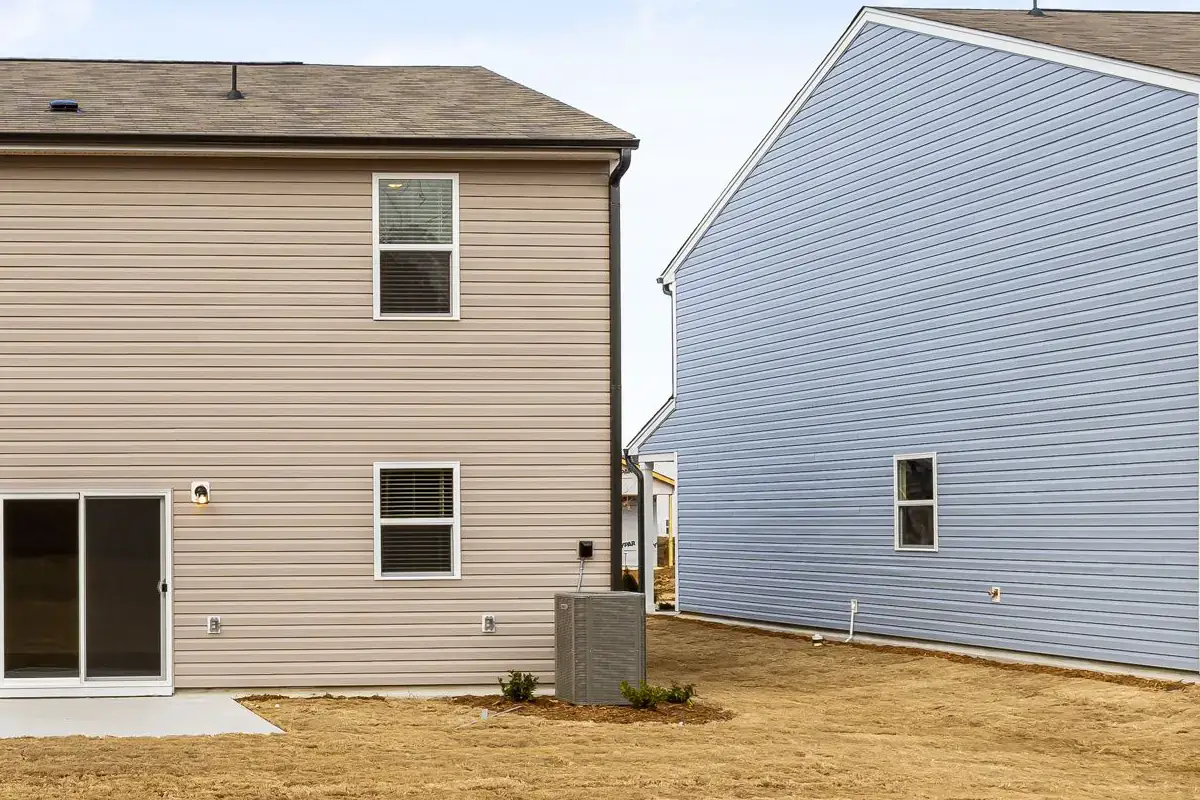Newly installed outdoor air conditioning unit on a small mulch bed behind a new two-story home