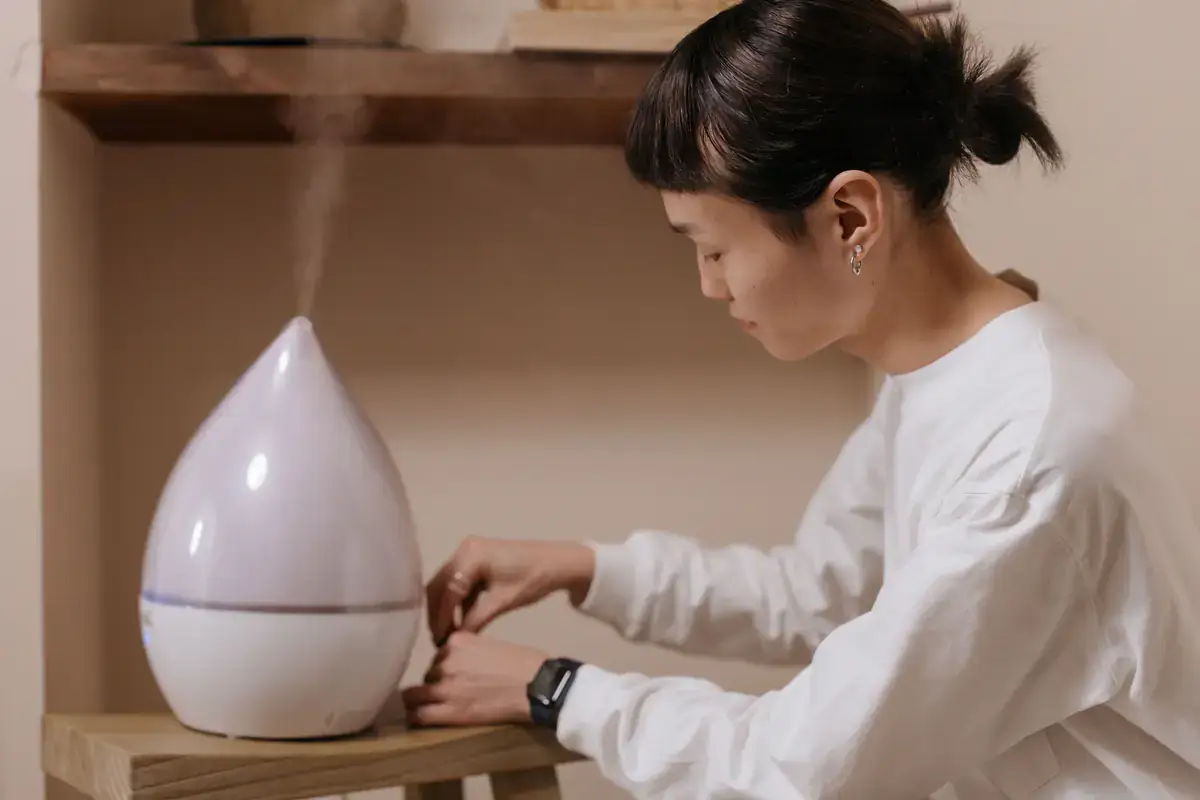 Person adjusting a white humidifier releasing mist on a wooden shelf