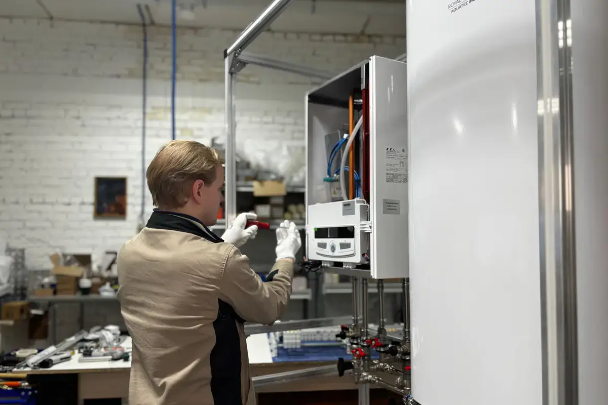 Technician in white gloves servicing a wall-mounted tankless heating unit in a workshop
