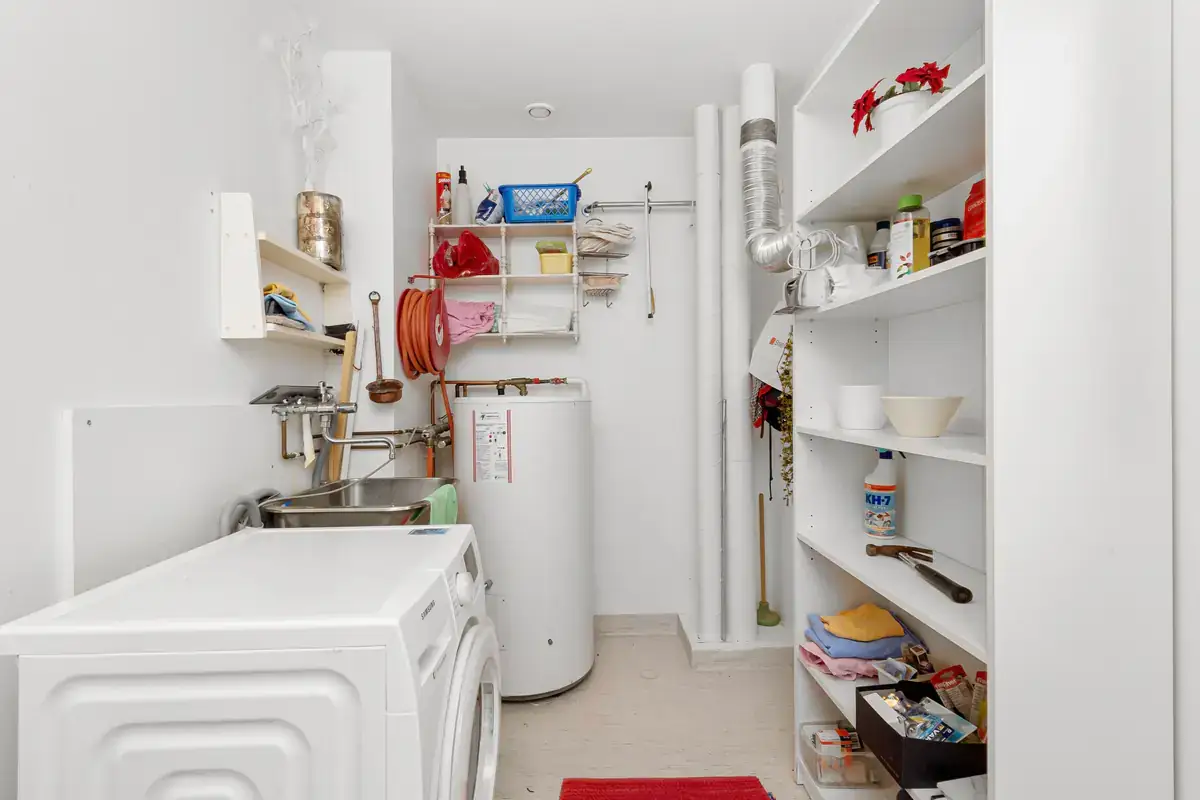 Tank water heater in a small laundry and storage room beside a washing machine